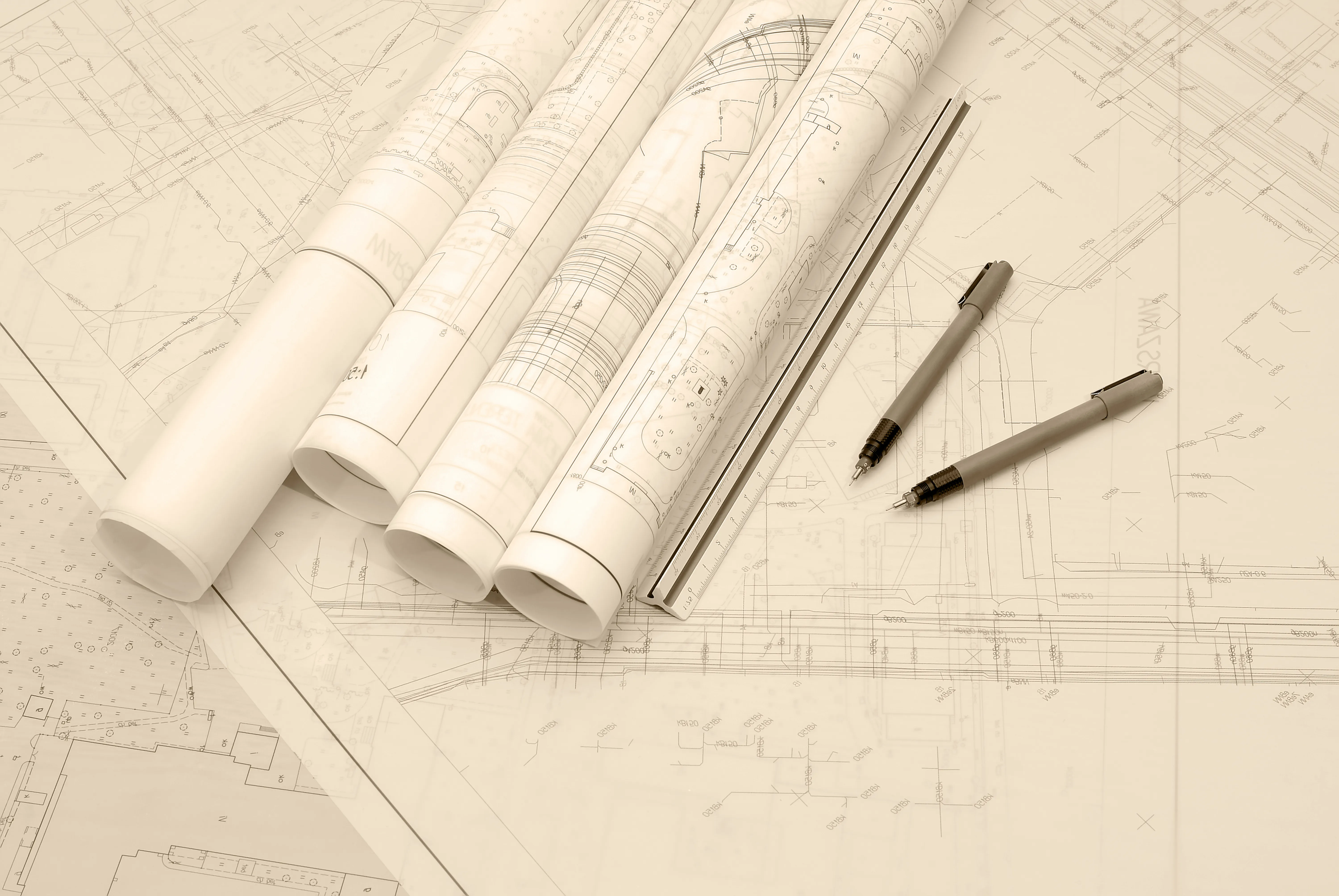 Rolled engineering blueprints with mechanical pencils and a ruler on a drafting surface.