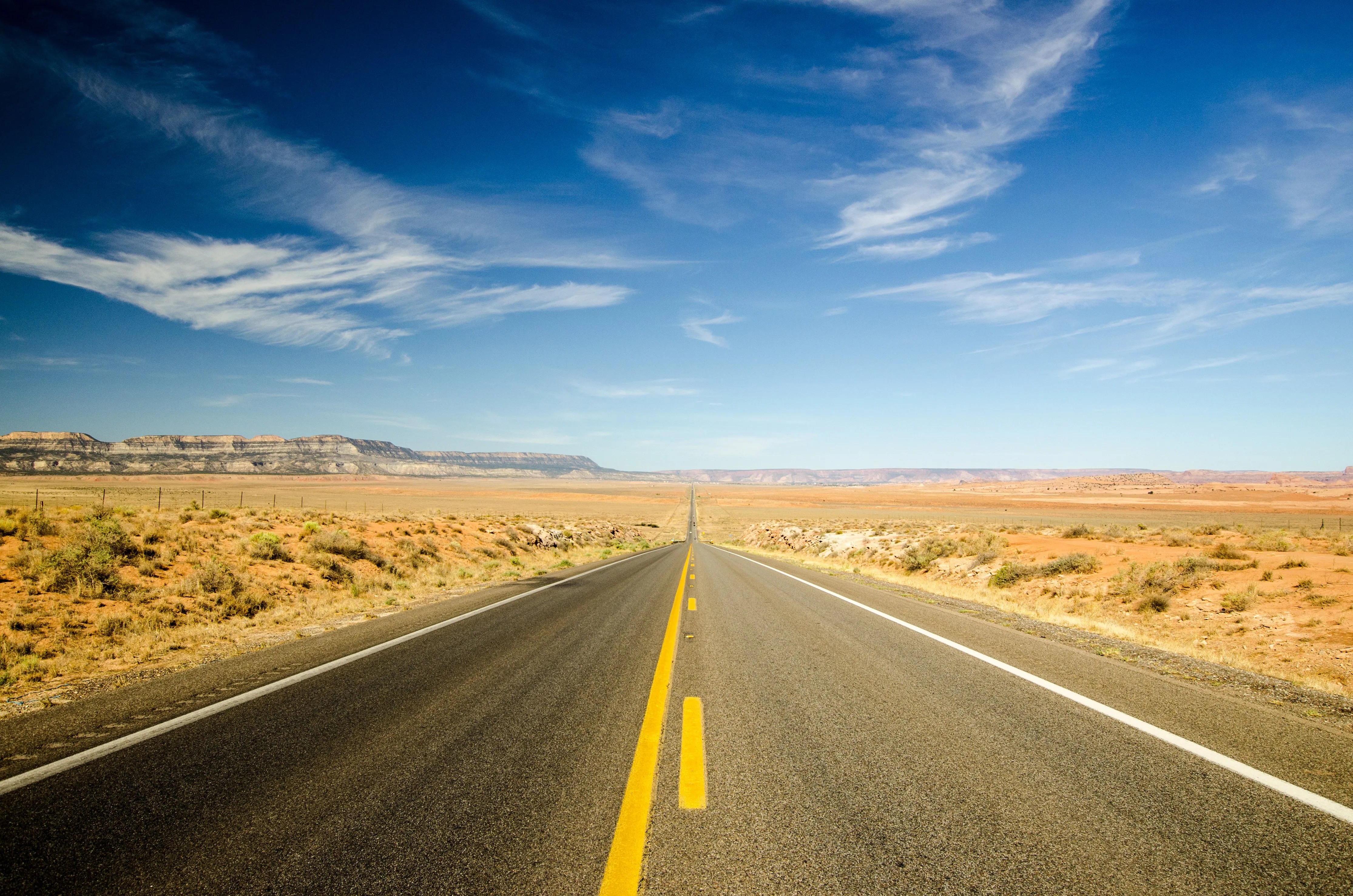 A long, straight West Texas highway running toward the horizon under a wide blue sky.