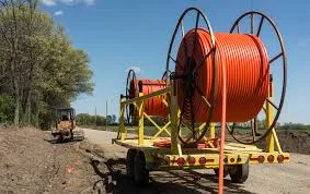 A large reel of orange fiber-optic cable on a trailer at a rural construction site.